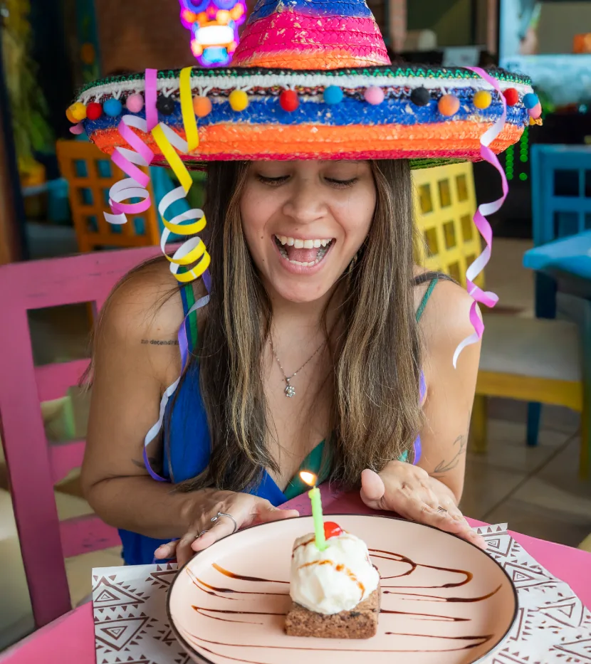 Clienta con sombrero de colores sorprendida frente a su postre de cumpleaños con vela